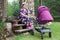 Portrait of happy smiling grandmother sitting on porch on summer sunny day with pram with newborn baby