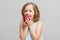 Portrait of a happy smiling little blonde girl on a gray background. Baby bites red apple