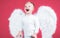 Portrait of happy smiling little curly blond Angel boy. Angelic child. Toddler wearing angel white dress costume and