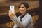 Portrait of happy, smiling woman sitting alone in the forest with smartphone. Millenial girl playing social media on