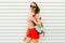 Portrait happy smiling young woman with backpack wearing red heart shaped sunglasses, shorts, white striped shirt on white wall