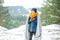 Portrait of happy teenage boy standing in park forest in snowy winter, holding red cup, freezing covered with blanket.