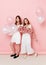 Portrait of happy two young women, dressed in a white, holdings a balloons, over pink background.