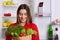 Portrait of happy woman with cheerful expression holds paper bag with tomatoes, cucmbers, dill and lettuce, comes from shop, going