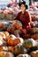 Portrait of happy woman with ripe orange pumpkin in hands on background of farmers market in brown sweater and hat. Cozy autumn