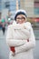 Portrait of happy woman in warm clothing standing arms crossed on city street