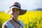 Portrait of happy woman wearing hat and standing in mustard field