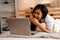 Portrait of happy young Asian girl in casual clothing lying down on bed while making a video call with laptop computer