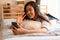 Portrait of happy young Asian girl in casual clothing lying down on bed while making a video call with smartphone and