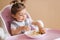 Portrait of happy young baby girl in high chair eating exotic fruits. Healthy nutrition for kids