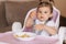 Portrait of happy young baby girl in high chair eating exotic fruits. Healthy nutrition for kids