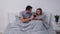 Portrait of happy young couple posing while lying in bedroom on bed. Man with passion plays game on mobile phone and