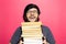 Portrait of happy young man holding bunch of books, wearing round eyeglasses on background of coral pink.