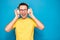 Portrait of happy young stylish man in yellow t-shirt, glasses and headphones expressing positivity isolated on blue background,