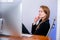 Portrait of happy young successful businesswoman at office. She sits at the table and looks at the display. Resting, leaning back