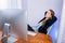 Portrait of happy young successful businesswoman at office. She sits at the table and looks at the display. Resting, leaning back