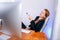 Portrait of happy young successful businesswoman at office. She sits at the table and looks at the display. Resting, leaning back