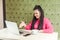 Portrait of happy young woman with black dreadlocks hairstyle in pink blouse sitting in and talking to webcamera at laptop and