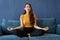 Portrait of healthy Asian woman meditating and exercise pose yoga on the sofa in morning. Zen relaxation and mindfulness lifestyle