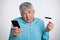 Portrait of hesitant grey haired mature male doesn`t know how to pay with credit card and make purchase online via internet with m