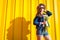 Portrait of hipster girl wearing glasses and hat with flowers against yellow background. Summer outfit. Fashion. Space