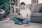 Portrait of his he nice attractive focused glad cheerful cheery guy sitting on carpet using cell browsing media