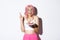 Portrait of hopeful birthday girl in pink wig, making wish with fingers crossed, holding b-day cake, standing over white