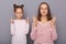 Portrait of hopeful brown haired woman and little girl with two hair buns posing isolated over gray background, keeps eyes closed