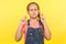 Portrait of hopeful cute little girl with braid in denim overalls crossing fingers for good luck, making childhood wishes