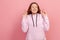 Portrait of hopeful joyous young woman with curly hair in hoodie raising fingers crossed while making wish, confident to win