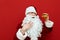 Portrait of hungry Santa Claus looking at burger in hand and stroking beard isolated red background.Funny man in Santa costume