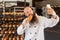 Portrait of hungry young adult blogger baker with long beard in white uniform standing in factory and making selfie on shelves