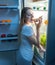 Portrait of hungry young woman taking pizza slice out of refrigerator and eating it. Concept of dieting and loosing