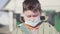 Portrait of ill Caucasian little boy in face mask rubbing eyes and sneezing. Close-up of sick child posing outdoors on