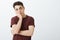 Portrait of impatient bored attractive guy in ordinary red t-shirt, leaning face on palm and looking up, waiting for end