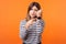 Portrait of impatient young woman with brown hair in long sleeve striped shirt. indoor studio shot isolated on orange background