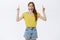 Portrait of impressed enthusiastic charming european female in yellow t-shirt and shorts raising arms pointing up and