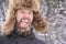 Portrait of an inadequate bearded man in a winter hat in a snowy forest grimaces, shows his tongue and drooling bubbles