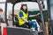 Portrait industrial female worker wearing a medical mask using a forklift in a warehouse wearing a yellow vest