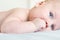 Portrait of infant kid lying on a bed. Close-up of healthy child sucking his fist. Focus on fist with blurred background. Baby te