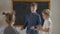 Portrait of intelligent genius schoolboy explaining mathematics to little children standing at chalkboard in classroom