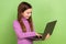 Portrait of intelligent schoolgirl with straight hair dressed pullover look at laptop typing message  on green