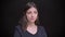 Portrait of irritated young caucasian long-haired brunette girl watching seriously into camera on black background.