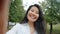 Portrait of joyful Asian girl making video call in green park smiling talking