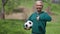 Portrait of joyful Caucasian senior woman holding soccer ball showing thumb up smiling. Cheerful fit retiree posing in