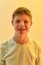 Portrait of joyful disabled boy with Down syndrome smiling at camera while posing  over yellow light background