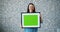 Portrait of joyful girl carrying green screen picture on brick wall background