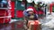 Portrait of joyful girl in Santa hat with gift box for Christmas on city street in winter with snow on festive market with decorat