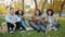 Portrait of joyful girls and guys singing playing the guitar on grass in city park