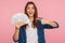 Portrait of joyful lucky girl in casual shirt happy to hold lot of money, pointing at dollar bills in hand and smiling